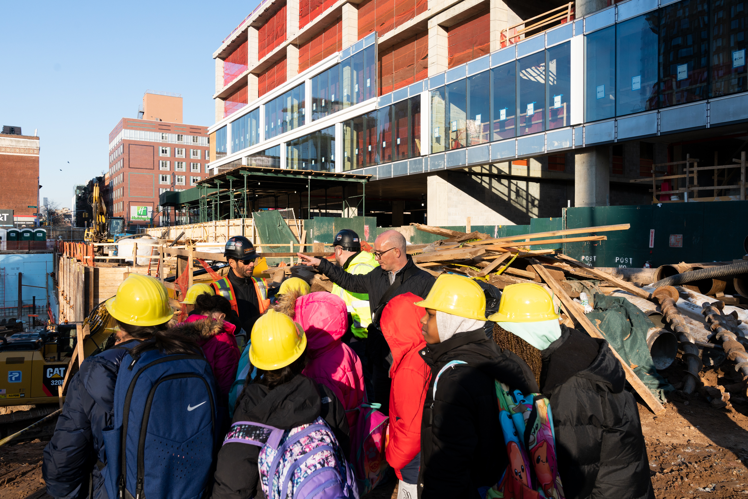 Students wearing hard hats tour the construction site at Essex Crossing